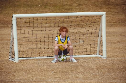 Girl in yellow scrimmage vest sitting on a football - Little Dribblers