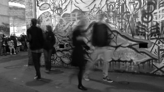 Trail of people walking past a graffitied wall long exposure monochrome