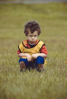 Curly haired boy squatting on field - Little Dribblers
