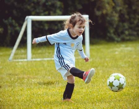 Little girl in German kit kicking football - Little Dribblers