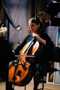 People playing cello and violin at a concert sitting on a chair in floral dress and black coat
