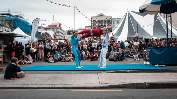 Children and parents watch an acrobatic performance in the street