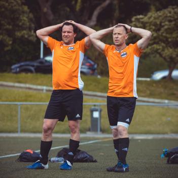 Two teammates in orange Adidas shirts putting hands on their heads - Sports Zone sunday league