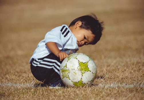 Little boy examining a football - Little Dribblers
