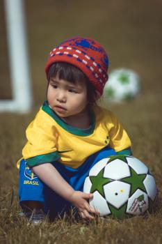 Little girl in Brasil kit picking up football - Little Dribblers