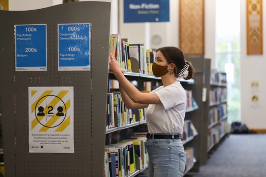 Young lady picking book from bookshelf