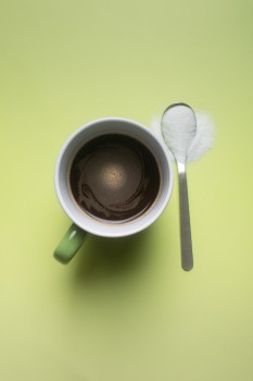 Stevia in a spoon next to a cup of coffee