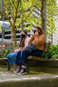 Masked young women sitting on a park bench