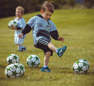 Boy wearing grey and black hoodie kicking football - Little Dribblers