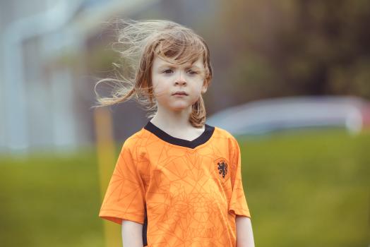 Girl in orange shirt and wind in hair at Little Dribblers football meet