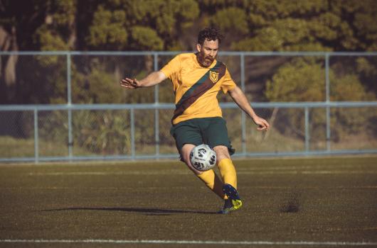 Bearded player kicks football lifting dirt from ground - Sports Zone sunday league