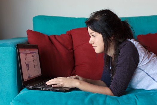 Teenage brunette uses laptop computer on sofa
