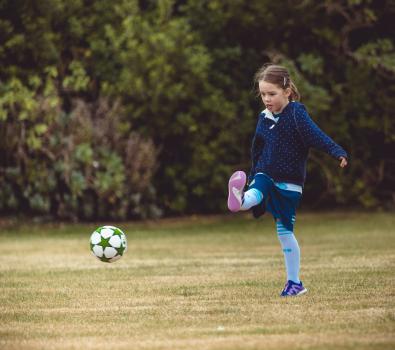 Girl in blue hoodie kicking football at Little Dribblers bout