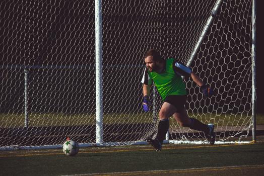 Goalkeeper wearing green scrimmage vest running after ball - Sports Zone sunday league