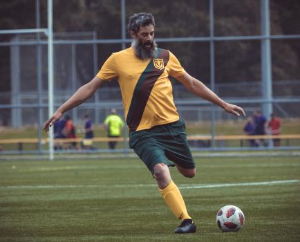 Bearded football player in yellow shirt kicking ball - Sports Zone sunday league
