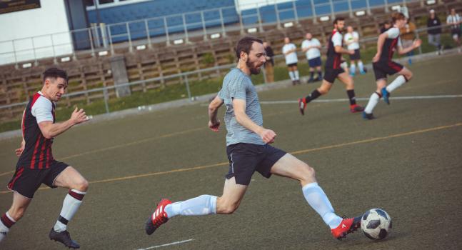 Player in a grey lined shirt running with the football - Sports Zone sunday league