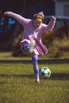 Girl in pink furry coat kicking football - Little Dribblers
