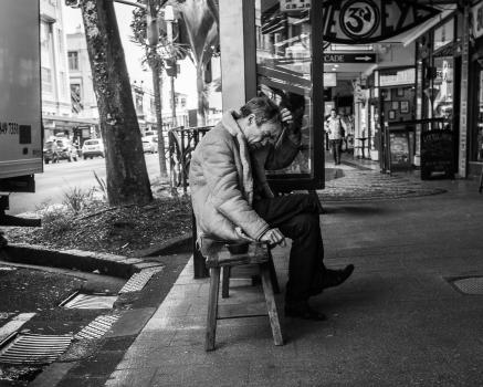 Old guy sitting in front of shops black and white