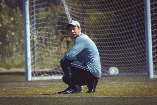 Goalkeeper in grey shirt sitting on grass at Sports Zone sunday league