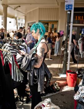 Tattooed cyan haired woman browsing for shirts at a market at Newtown festival 2021