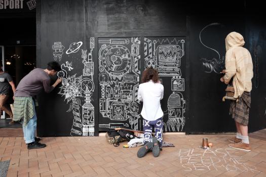 Artists chalk drawing black wall on Cuba Street