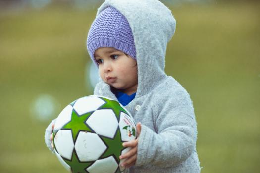 Little girl in grey hoodie carrying football Little Dribblers