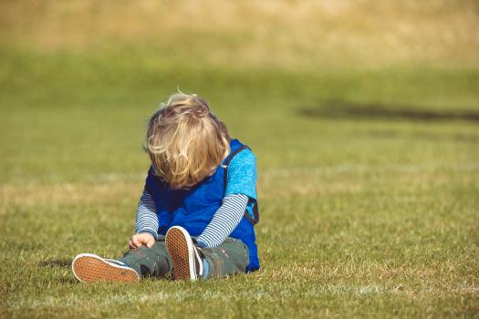 Kid wearing blue scrimmage vest sitting on grass - Little Dribblers