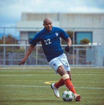 Dark skinned bald football player in blue shirt - Sports Zone sunday league