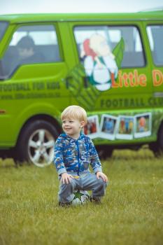Blonde haired kid with camouflage jacket sitting on football - Little Dribblers