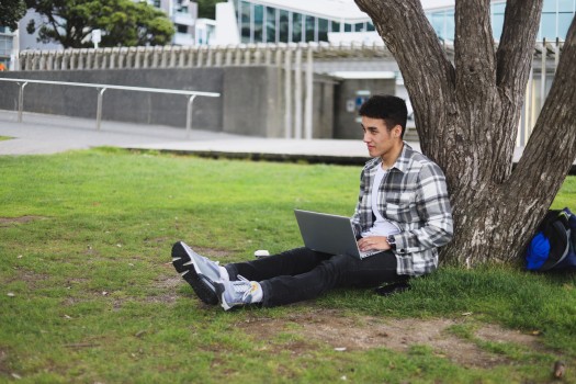 Young man with laptop under a tree