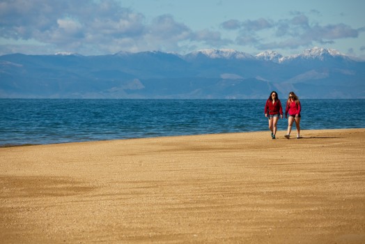 Teenage girls walk sandy shore, Abel Tasman 