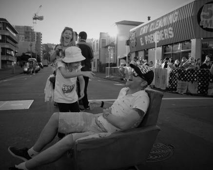 Family laughing with father sitting on a chair in the middle of a street black and white