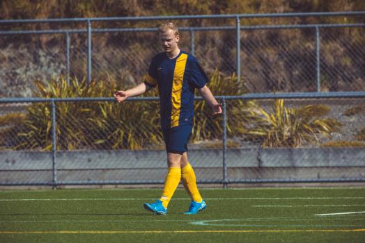 Football player in blue and yellow kit walking on field - Sports Zone sunday league