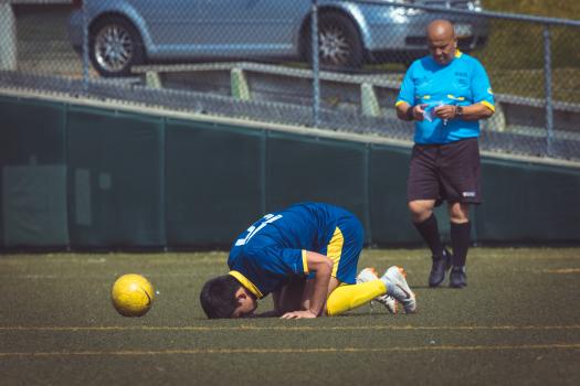 Footballer bow down to earth next to yellow Nike football - Sports Zone sunday league
