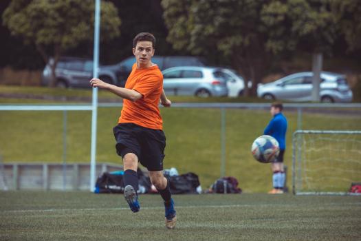 Player in orange shirt kicks football bokeh - Sports Zone sunday league