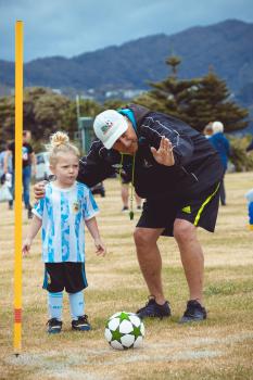 Coach guiding little girl in Argentine kit where to kick football