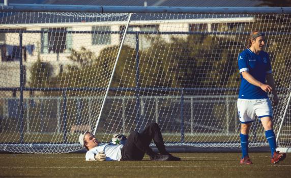 Goalkeeper lying on the grass holding football - Sports Zone sunday league