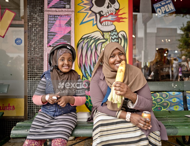 Hijab wearing mother and daughter on a bench eating corn at Newtown festival 2021