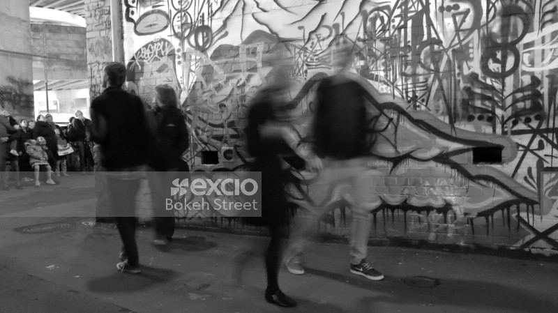 Trail of people walking past a graffitied wall long exposure monochrome
