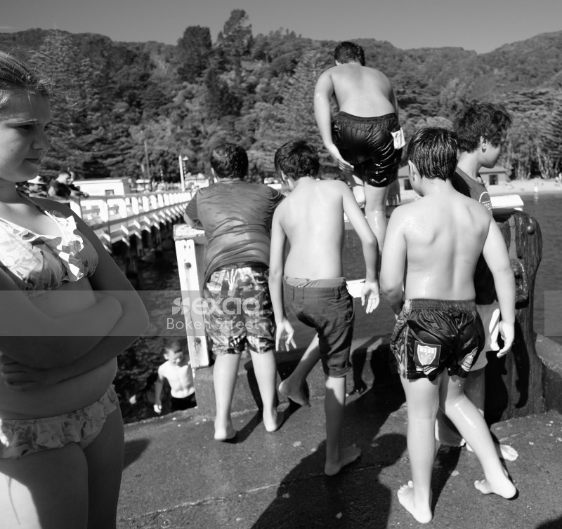 Kids jumping into the water from wharf in Days bay black and white