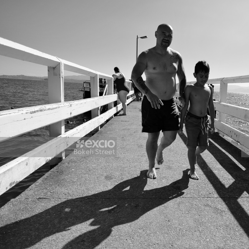 Father and son walking on a pier in their swimming trunks in Days bay monochrome