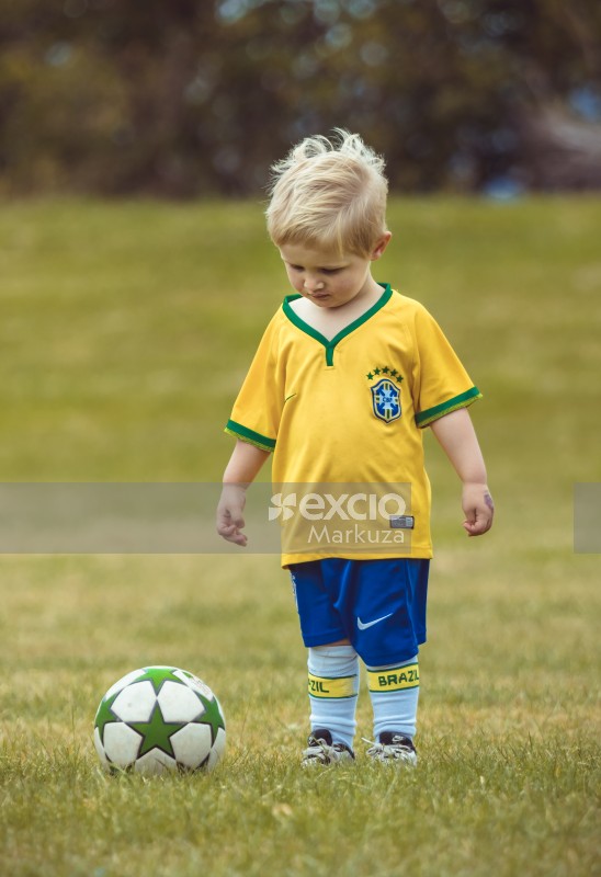 Little blonde boy in Brasil kit looking at football - Little Dribblers
