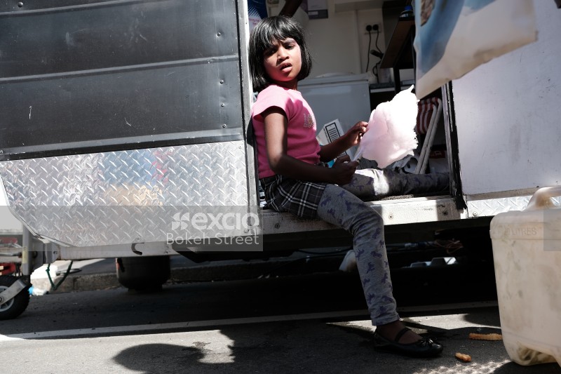 Little girl sitting in the door of a food truck eating cotton candy at Newtown festival 2021