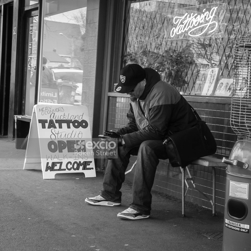 Guy sitting on a bench at Ponsonby street outside a tattoo studio