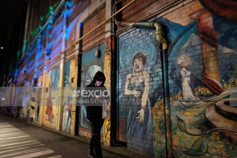 Guy walking past a wall with artwork at night