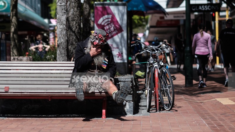 Guy on bench next to bicycles wearing a hat with ribbons