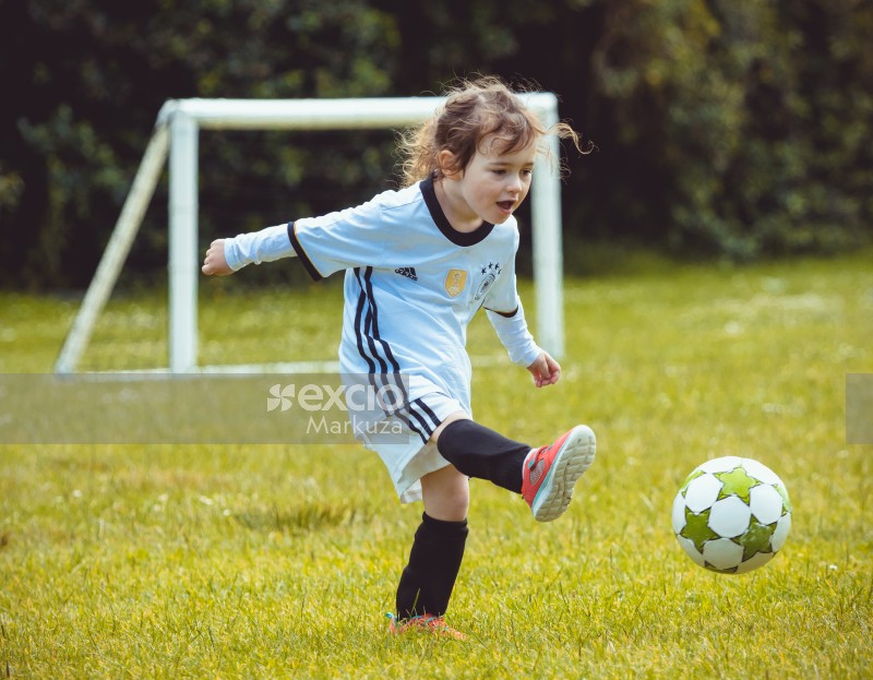 Little girl in German kit kicking football - Little Dribblers