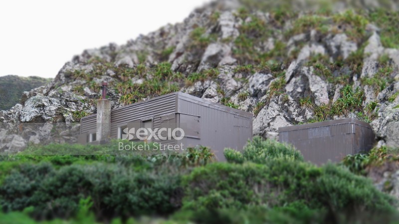 Grey shack on beach at higher ground surrounded by mountains and foliage
