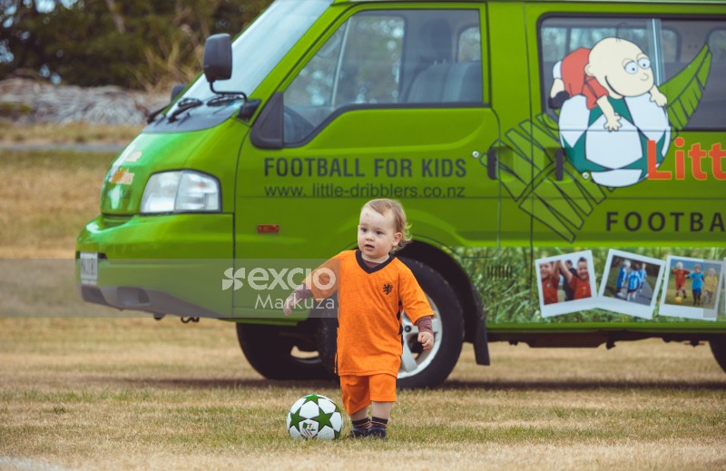 Kid in Netherland kit in front of a green van at Little Dribblers play