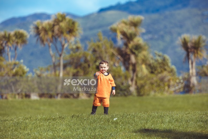 Little boy in orange kit waving at camera bokeh
